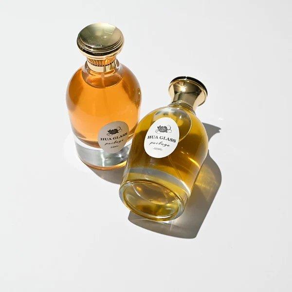 HUA0254 perfume bottle, rounded transparent glass body with smooth curved silhouette and thick base, 100 ml liquid, flared cylindrical Zamac cap with glossy finish, available in ribbed side texture or smooth side surface style, printed logo on bottle, elegant modern luxury design, ideal for gifting and daily use.