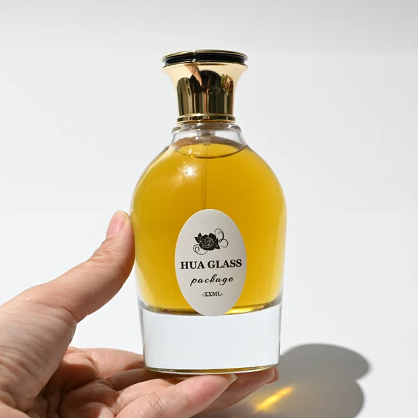 HUA0254 perfume bottle, rounded transparent glass body with smooth curved silhouette and thick base, 100 ml liquid, flared cylindrical Zamac cap with glossy finish, available in ribbed side texture or smooth side surface style, printed logo on bottle, elegant modern luxury design, ideal for gifting and daily use.