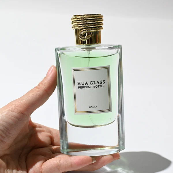 HUA0256 perfume bottle, transparent glass body with rectangular paper bag-inspired silhouette, smooth curved shoulders and oval thick base, 80 ml liquid, cylindrical plastic cap with layered ring texture and metallic glossy finish, printed logo label, modern luxury design, ideal for gifting and daily use.