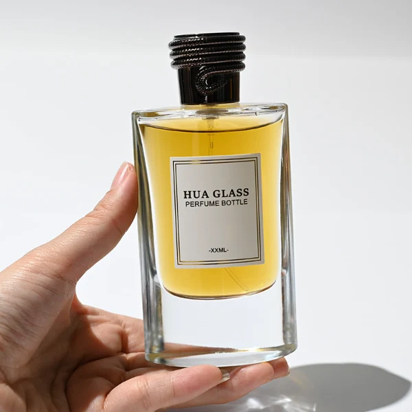 HUA0256 perfume bottle, transparent glass body with rectangular paper bag-inspired silhouette, smooth curved shoulders and oval thick base, 80 ml liquid, cylindrical plastic cap with layered ring texture and metallic glossy finish, printed logo label, modern luxury design, ideal for gifting and daily use.