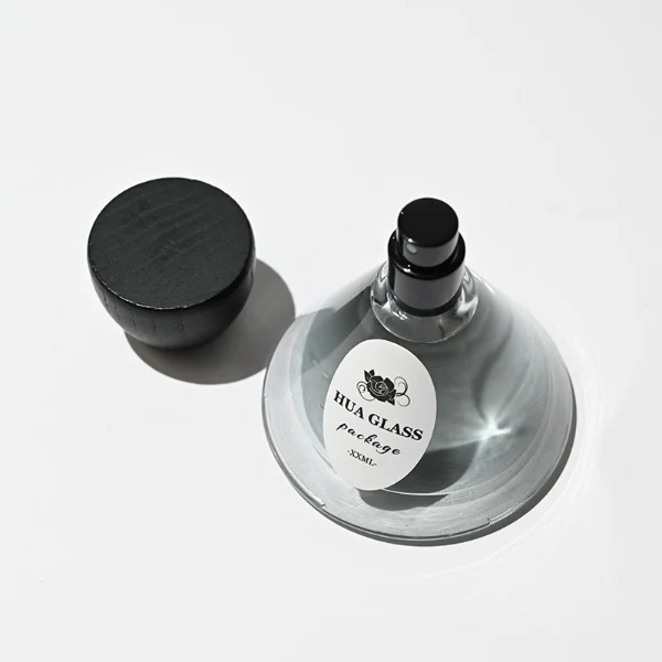 HUA0257 perfume bottle, transparent glass body with wide cone-shaped silhouette and thick rounded base, 30 ml, 50 ml, or 100 ml liquid, rounded wooden cap with matte finish and bowl-shaped silhouette in black or brown color, printed logo label, artistic modern luxury design, ideal for gifting and daily use.