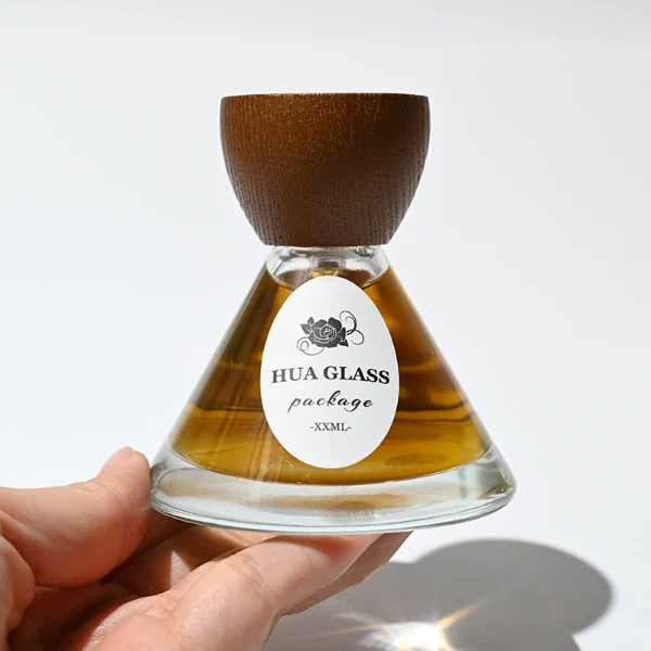 HUA0257 perfume bottle, transparent glass body with wide cone-shaped silhouette and thick rounded base, 30 ml, 50 ml, or 100 ml liquid, rounded wooden cap with matte finish and bowl-shaped silhouette in black or brown color, printed logo label, artistic modern luxury design, ideal for gifting and daily use.