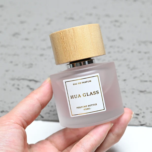 HUA0263 perfume bottle, frosted cylindrical glass body with thick rounded base, 30 ml, 50 ml, or 100 ml liquid, flat cylindrical bamboo cap with natural wood grain texture and silver bottle neck, printed logo label, natural minimalist luxury design, ideal for gifting and daily use.