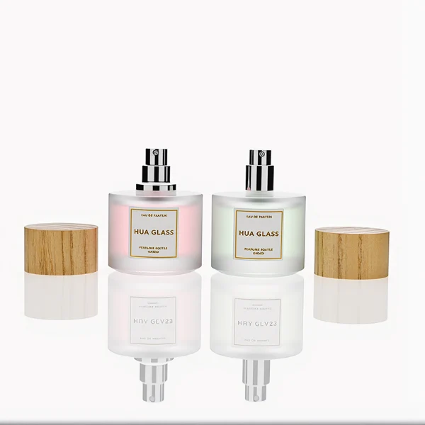 HUA0263 perfume bottle, frosted cylindrical glass body with thick rounded base, 30 ml, 50 ml, or 100 ml liquid, flat cylindrical bamboo cap with natural wood grain texture and silver bottle neck, printed logo label, natural minimalist luxury design, ideal for gifting and daily use.