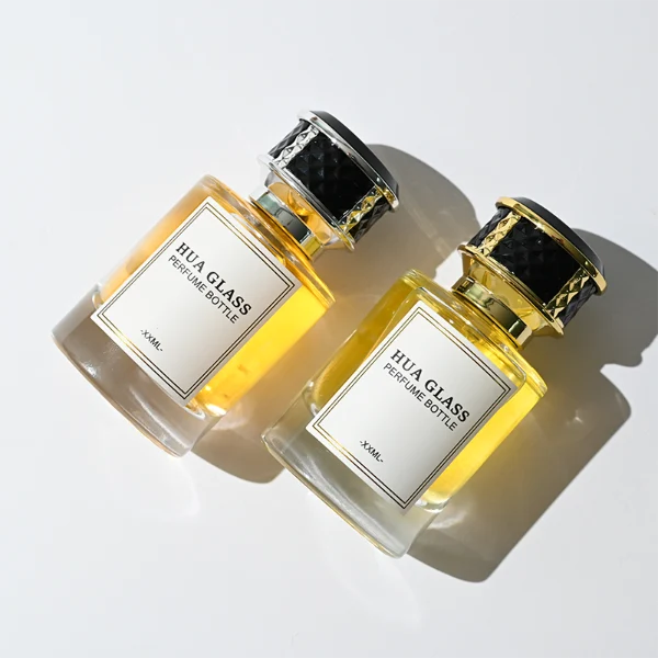 HUA0267 perfume bottle, cylindrical transparent glass body with thick rounded base, 30 ml, 50 ml, or 100 ml liquid, flat cylindrical plastic cap with faceted lattice side texture and gold or silver metallic striped decoration, printed logo label, modern luxury elegance design, ideal for gifting and daily use.