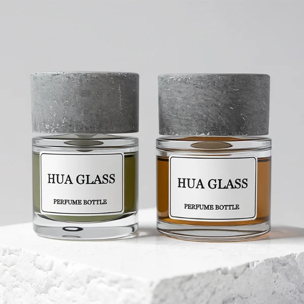 HUA0268 perfume bottle, cylindrical transparent glass body with thick rounded base, 30 ml, 50 ml, or 100 ml liquid, oversized flat cylindrical artificial stone cap with matte stone texture, printed logo label, contemporary minimalist luxury design, ideal for gifting and daily use.