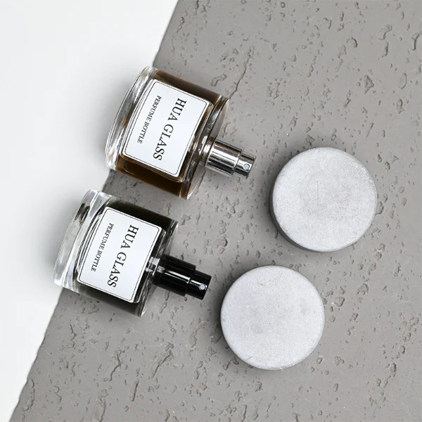 HUA0268 perfume bottle, cylindrical transparent glass body with thick rounded base, 30 ml, 50 ml, or 100 ml liquid, oversized flat cylindrical artificial stone cap with matte stone texture, printed logo label, contemporary minimalist luxury design, ideal for gifting and daily use.