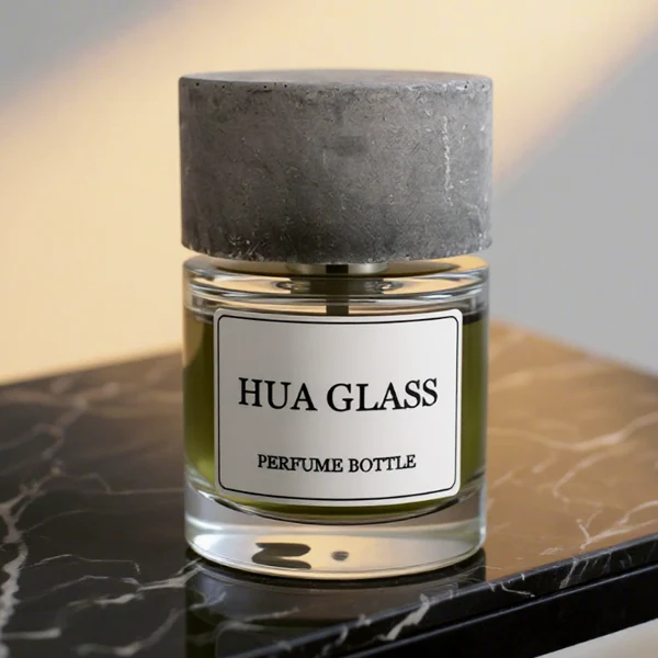 HUA0268 perfume bottle, cylindrical transparent glass body with thick rounded base, 30 ml, 50 ml, or 100 ml liquid, oversized flat cylindrical artificial stone cap with matte stone texture, printed logo label, contemporary minimalist luxury design, ideal for gifting and daily use.