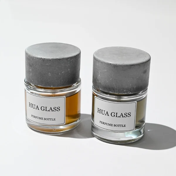 HUA0268 perfume bottle, cylindrical transparent glass body with thick rounded base, 30 ml, 50 ml, or 100 ml liquid, oversized flat cylindrical artificial stone cap with matte stone texture, printed logo label, contemporary minimalist luxury design, ideal for gifting and daily use.