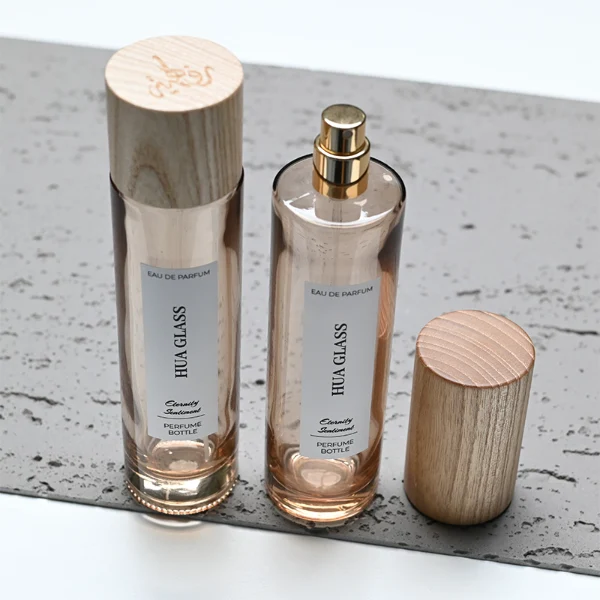HUA0269 perfume bottle, slim cylindrical transparent glass body with rounded base, 30 ml, 50 ml, or 100 ml liquid, tall cylindrical wooden cap with natural wood grain texture, printed vertical logo label, natural minimalist elegance design, ideal for gifting and travel use.
