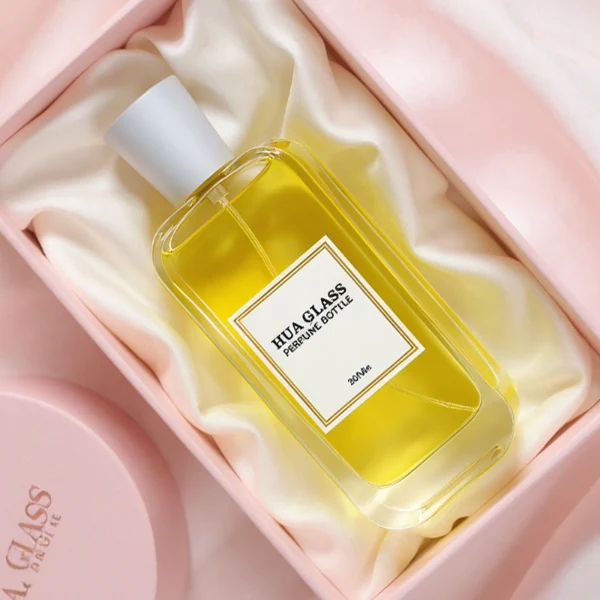 HUA0270 perfume bottle, rounded rectangular transparent glass body with smooth curved corners and thick base, 50 ml or 100 ml liquid, tapered cylindrical plastic cap in glossy black or white finish, printed logo label, modern elegant luxury design, ideal for gifting and daily use.