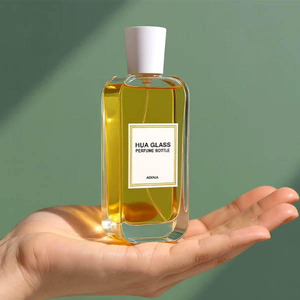 HUA0270 perfume bottle, rounded rectangular transparent glass body with smooth curved corners and thick base, 50 ml or 100 ml liquid, tapered cylindrical plastic cap in glossy black or white finish, printed logo label, modern elegant luxury design, ideal for gifting and daily use.