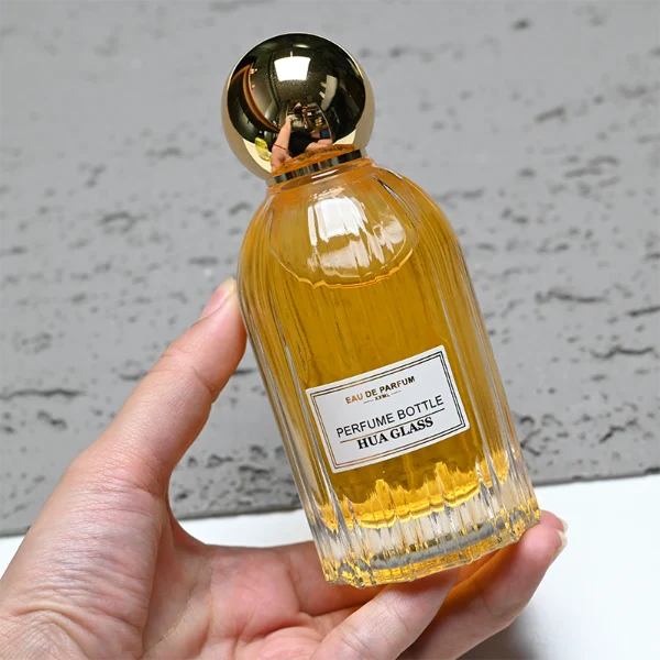 HUA0271 perfume bottle, cylindrical transparent glass body with vertical fluted texture and thick rounded base, 100 ml liquid, oversized spherical magnetic cap with glossy black or gold mirror finish, printed logo label, vintage luxury elegance design, ideal for gifting and daily use.
