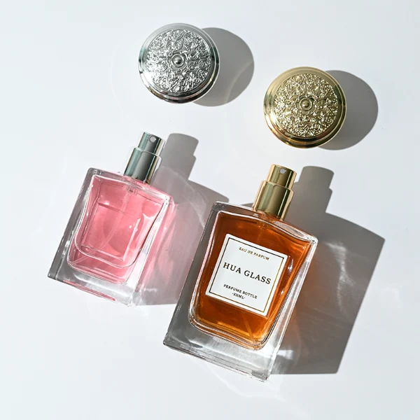 HUA0273 perfume bottle, transparent rectangular glass body with beveled edges and thick base, 50 ml or 100 ml liquid, glossy bowl-shaped plastic cap in silver or gold with matching bottle neck, brand label attached on bottle surface, modern elegant luxury design, ideal for gifting and daily use.