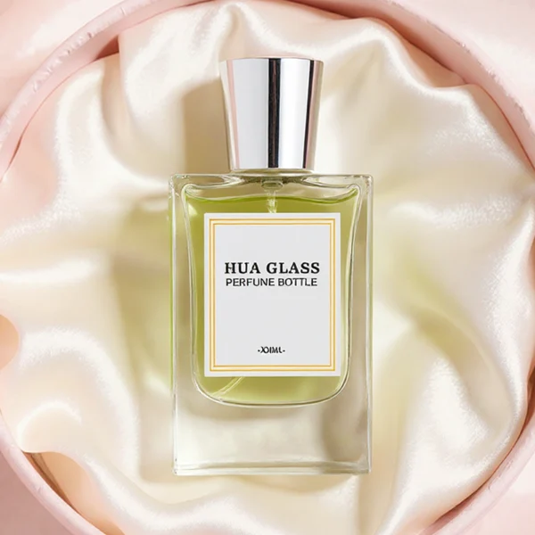 HUA0274 perfume bottle, transparent colorless rectangular glass body with rounded shoulders and thick base, 30 ml, 50 ml, or 100 ml liquid, glossy tapered cylindrical plastic cap in gold, silver, or white, printed label attached on bottle surface, modern minimalist luxury design, ideal for gifting and daily use.
