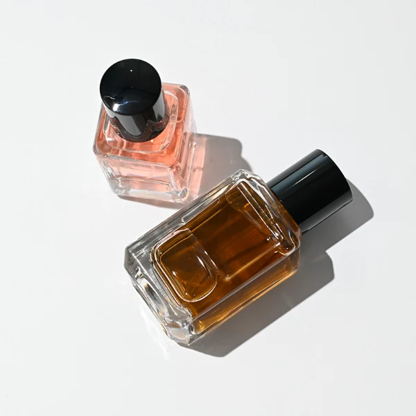 HUA0275 perfume bottle, transparent colorless octagonal glass body with beveled edges and thick base, 30 ml or 50 ml liquid, glossy black cylindrical plastic cap with flat top, aluminum label/sticker attached on bottle surface, modern minimalist luxury design, ideal for gifting and daily use.