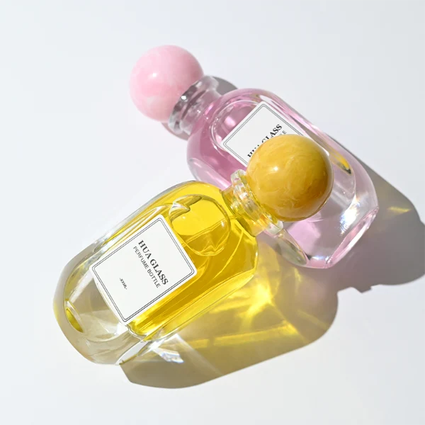 HUA0276 perfume bottle, transparent colorless oval glass body with rounded contours and thick base, 80 ml liquid, glossy spherical resin cap with marble-like texture in customizable colors, printed label attached on bottle surface, modern elegant luxury design, ideal for gifting and daily use.