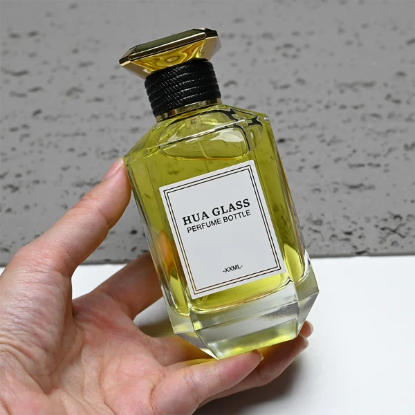 HUA0279 perfume bottle, transparent or customizable gradient geometric glass body with thick base and beveled edges, 30 ml, 50 ml, or 100 ml liquid, flat diamond-top threaded plastic cap in black or gold finish, printed logo label attached on bottle surface, modern luxury fashion design, ideal for gifting and daily use.