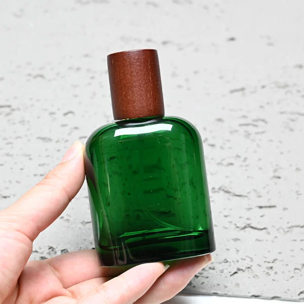 HUA0281 perfume bottle, rounded rectangular customizable semi-transparent glass body in amber, black, or green with thick base, 50 ml liquid, cylindrical cap in natural wood, dark brown wood, or black finish, gold printed logo on bottle surface, modern vintage luxury design, ideal for gifting and daily use.