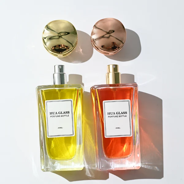 HUA0284 perfume bottle, rectangular transparent colorless glass body with thick base and beveled edges, 100 ml liquid, cylindrical glossy plastic cap with wave-pattern side texture in gold or rose gold finish, printed label attached on bottle surface, modern luxurious fashion design, ideal for gifting and daily use.