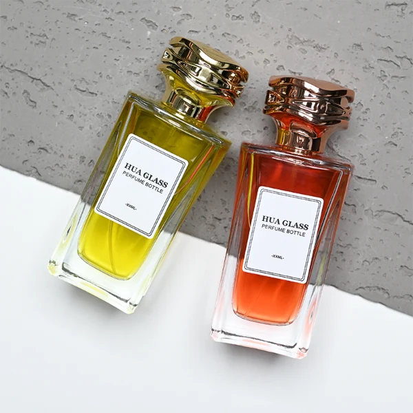 HUA0284 perfume bottle, rectangular transparent colorless glass body with thick base and beveled edges, 100 ml liquid, cylindrical glossy plastic cap with wave-pattern side texture in gold or rose gold finish, printed label attached on bottle surface, modern luxurious fashion design, ideal for gifting and daily use.