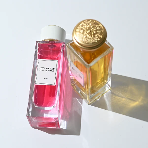 HUA0285 perfume bottle, tall rectangular transparent colorless glass body with thick base and flat sides, label attached on bottle surface, 100 ml liquid, cylindrical plastic cap with white or gold mesh-textured surface and gold or black rings on both ends, modern minimalist luxury design, ideal for gifting and daily use.