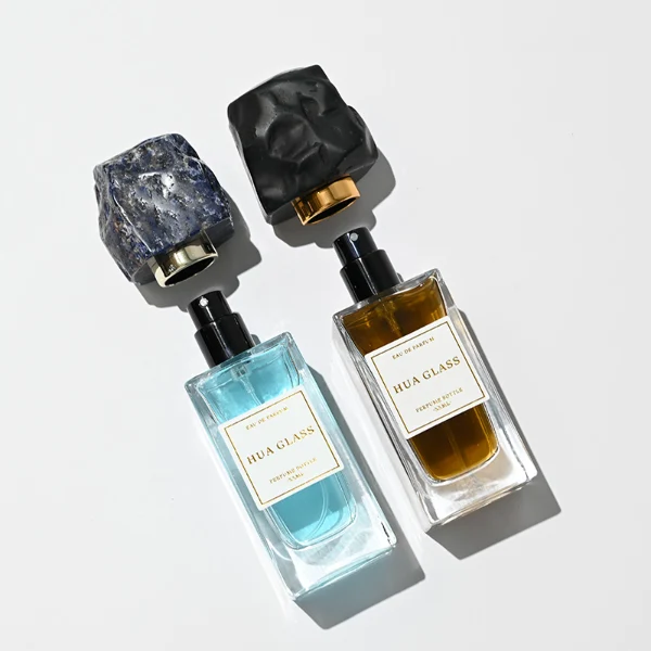 HUA0286 perfume bottle, rectangular transparent colorless glass body with thick base and beveled edges, 30 ml, 50 ml, or 100 ml liquid, irregular natural stone cap with raw textured surface and gold bottle neck, printed label attached on bottle surface, modern artistic luxury design, ideal for gifting and daily use.