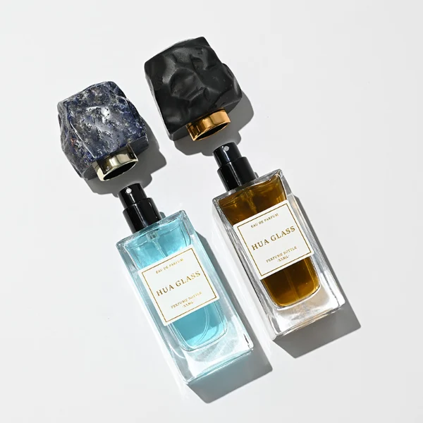 HUA0286 perfume bottle, rectangular transparent colorless glass body with thick base and beveled edges, 30 ml, 50 ml, or 100 ml liquid, irregular natural stone cap with raw textured surface and gold bottle neck, printed label attached on bottle surface, modern artistic luxury design, ideal for gifting and daily use.