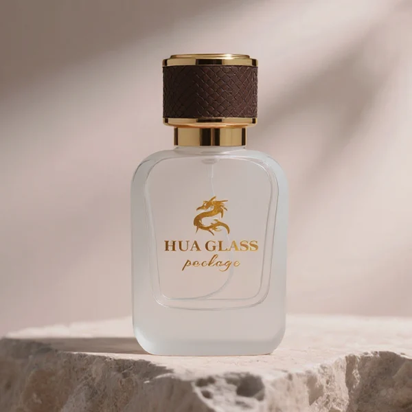 HUA0288 perfume bottle, rounded rectangular transparent or customizable semi-transparent glass body with thick base, 30 ml, 50 ml, or 100 ml liquid, cylindrical gold plastic cap wrapped with mesh-textured leather and gold bottle neck, gold printed logo on bottle surface, modern luxurious fashion design, ideal for gifting and daily use.