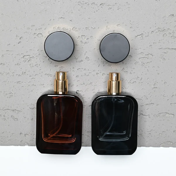 HUA0289 perfume bottle, rounded rectangular semi-transparent black or red glass body with thick base and smooth edges, 30 ml, 50 ml, or 100 ml liquid, black cylindrical plastic cap with diagonal gold accent and gold bottle neck, gold printed logo on bottle surface, modern luxurious fashion design, ideal for gifting and daily use.