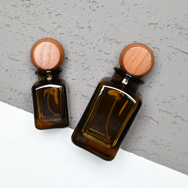 HUA0290 perfume bottle, rounded rectangular semi-transparent amber glass body with thick base and smooth edges, 30 ml, 50 ml, or 100 ml liquid, flattened spherical wooden cap with natural wood texture, gold printed logo on bottle surface, modern vintage luxury design, ideal for gifting and daily use.