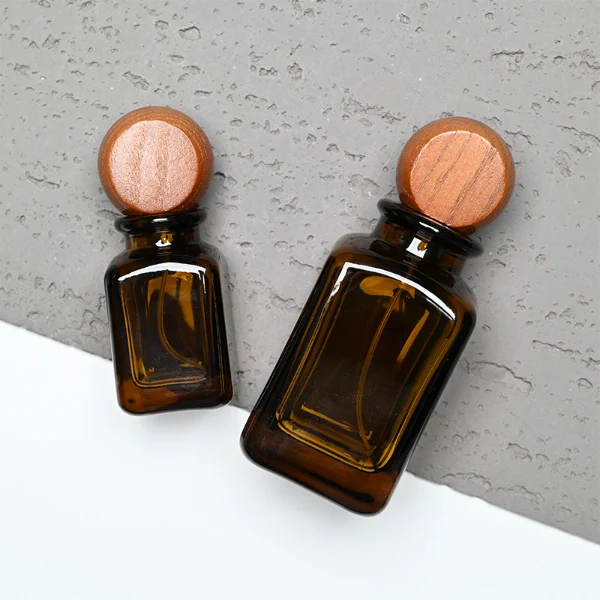 HUA0290 perfume bottle, rounded rectangular semi-transparent amber glass body with thick base and smooth edges, 30 ml, 50 ml, or 100 ml liquid, flattened spherical wooden cap with natural wood texture, gold printed logo on bottle surface, modern vintage luxury design, ideal for gifting and daily use.