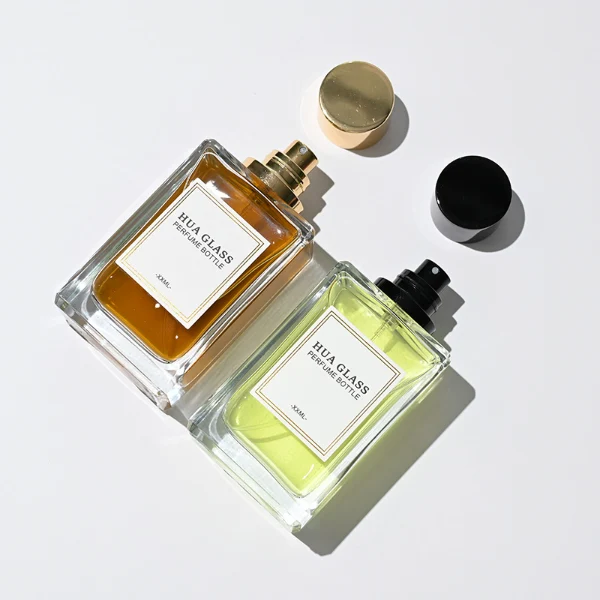 HUA0291 perfume bottle, rectangular transparent colorless glass body with thick base and beveled edges, 100 ml liquid, glossy cylindrical aluminum cap in gold or black finish, printed label attached on bottle surface, modern minimalist luxury design, ideal for gifting and daily use.
