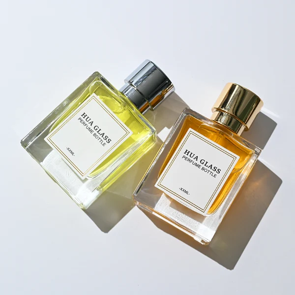 HUA0294 perfume bottle, square transparent colorless glass body with thick base and beveled edges, 50 ml liquid, glossy cylindrical Zamac cap in black, gold, or silver finish with matching bottle neck, printed label attached on bottle surface, modern minimalist luxury design, ideal for gifting and daily use.