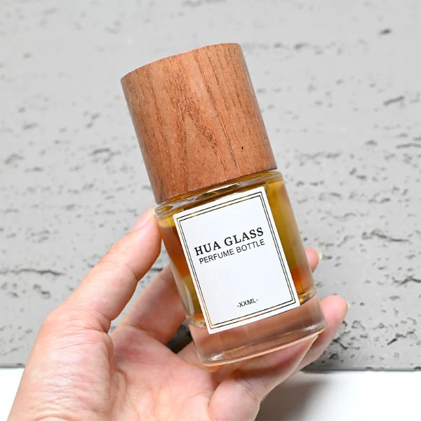 HUA0296 perfume bottle, cylindrical transparent colorless glass body with thick base and smooth rounded silhouette, 30 ml, 50 ml, or 100 ml liquid, cylindrical wooden cap in natural wood or matte black finish, printed label attached on bottle surface, modern minimalist luxury design, ideal for gifting and daily use.