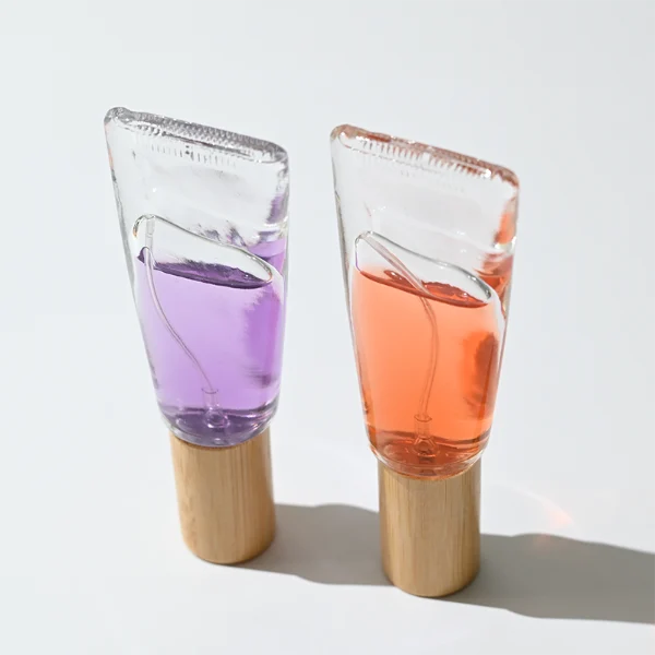 HUA0297 perfume bottle, transparent colorless cosmetic tube-inspired glass body with asymmetrical sculptural silhouette and bamboo base, 10 ml liquid, integrated natural bamboo cap, clean glass surface without logo printing, artistic modern minimalist design, ideal for travel and gifting.