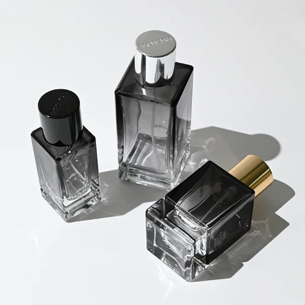 HUA0298 perfume bottle, gradient semi-transparent glass body with thick base and curved side contours, 30 ml, 50 ml, or 100 ml liquid, glossy cylindrical aluminum cap in black, silver, or gold finish, printed logo on bottle surface, modern minimalist luxury design, ideal for gifting and daily use.