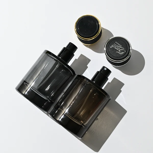 HUA0301 perfume bottle, semi-transparent black cylindrical glass body with thick base, 30 ml, 50 ml, or 100 ml liquid, black leather-wrapped plastic cap with gold or silver plastic bottle neck, gold or silver printed logo on bottle surface, modern masculine luxury design, ideal for gifting and daily use.