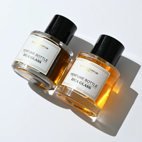 HUA0303 perfume bottle, cylindrical transparent colorless glass body with thick rounded base and smooth curved silhouette, 30 ml, 50 ml, or 100 ml liquid, glossy black cylindrical aluminum cap with flat top, printed label attached on bottle surface, modern minimalist luxury design, ideal for gifting and daily use.
