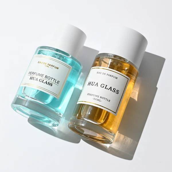 HUA0304 perfume bottle, cylindrical transparent colorless glass body with thick rounded base and smooth curved silhouette, 30 ml, 50 ml, or 100 ml liquid, glossy white cylindrical plastic cap with flat top, printed label attached on bottle surface, modern minimalist luxury design, ideal for gifting and daily use.