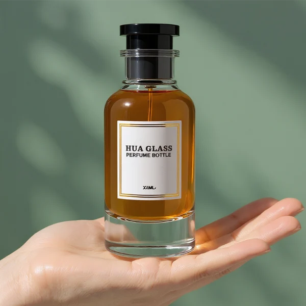 HUA0305 perfume bottle, cylindrical transparent colorless glass body with thick rounded base and curved shoulders, 50 ml or 100 ml liquid, stopper-shaped cylindrical plastic cap in black or white finish, printed label attached on bottle surface, modern minimalist luxury design, ideal for gifting and daily use.
