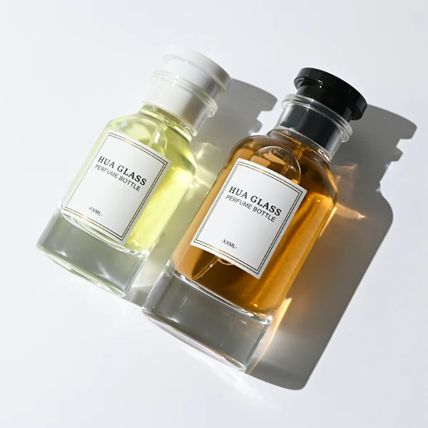 HUA0305 perfume bottle, cylindrical transparent colorless glass body with thick rounded base and curved shoulders, 50 ml or 100 ml liquid, stopper-shaped cylindrical plastic cap in black or white finish, printed label attached on bottle surface, modern minimalist luxury design, ideal for gifting and daily use.