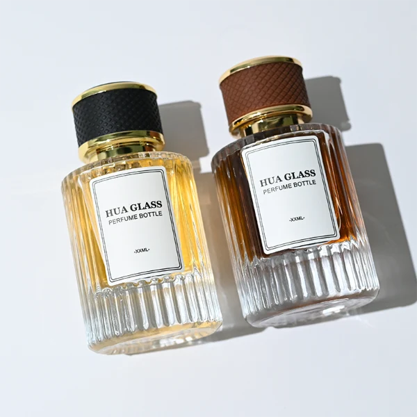 HUA0307 perfume bottle, cylindrical transparent colorless glass body with vertical ribbed texture and thick base, 30 ml, 50 ml, or 100 ml liquid, gold plastic cylindrical cap wrapped with black or brown leather, printed label attached on bottle surface, modern vintage luxury design, ideal for gifting and daily use.