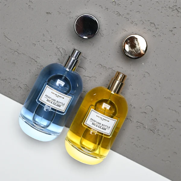 HUA0310 perfume bottle, rounded transparent colorless glass body with thick base and smooth curved silhouette, 100 ml liquid, glossy cylindrical Zamac cap with matching gold or silver metallic gloss bottle neck, printed label attached on bottle surface, modern minimalist luxury design, ideal for gifting and daily use.