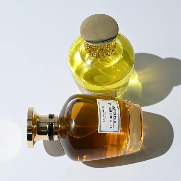 HUA0314 perfume bottle, rounded transparent colorless glass body with thick base and smooth curved silhouette, 100 ml liquid, ornamental Zamak cap with carved crown-inspired or layered dome design in glossy gold finish, printed label attached on bottle surface, vintage royal luxury design, ideal for gifting and daily use.