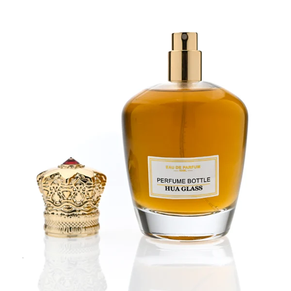 HUA0314 perfume bottle, rounded transparent colorless glass body with thick base and smooth curved silhouette, 100 ml liquid, ornamental Zamak cap with carved crown-inspired or layered dome design in glossy gold finish, printed label attached on bottle surface, vintage royal luxury design, ideal for gifting and daily use.