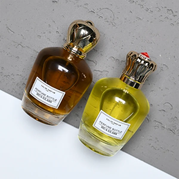 HUA0314 perfume bottle, rounded transparent colorless glass body with thick base and smooth curved silhouette, 100 ml liquid, ornamental Zamak cap with carved crown-inspired or layered dome design in glossy gold finish, printed label attached on bottle surface, vintage royal luxury design, ideal for gifting and daily use.