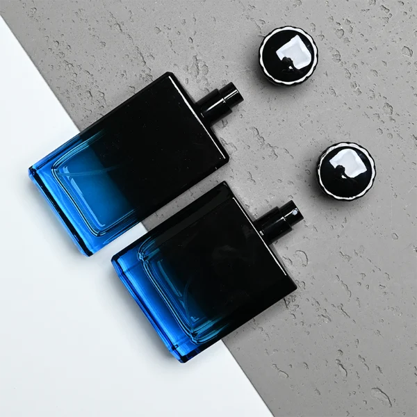 HUA0315 perfume bottle, rectangular semi-transparent glass body with blue-to-black gradient color, thick base and sharp edges, 50 ml or 100 ml liquid, textured cylindrical black plastic cap with layered neck detail, aluminum label/sticker attached on bottle surface, modern masculine luxury design, ideal for gifting and daily use.