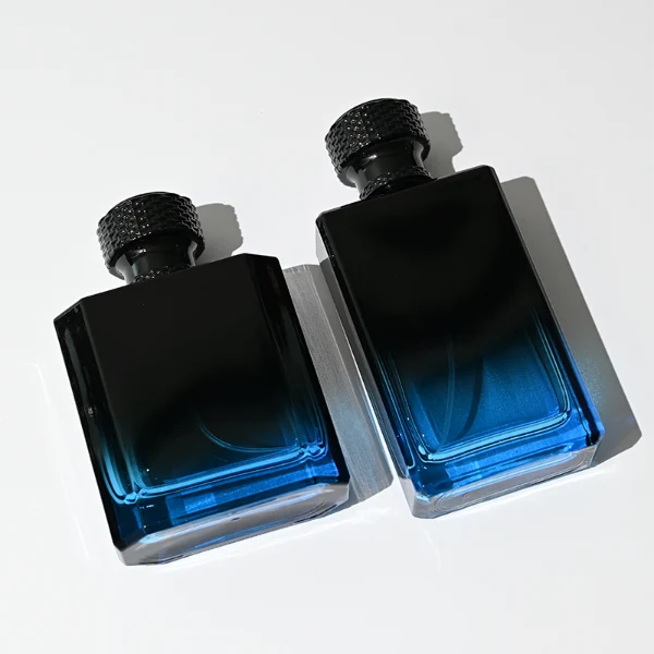HUA0315 perfume bottle, rectangular semi-transparent glass body with blue-to-black gradient color, thick base and sharp edges, 50 ml or 100 ml liquid, textured cylindrical black plastic cap with layered neck detail, aluminum label/sticker attached on bottle surface, modern masculine luxury design, ideal for gifting and daily use.