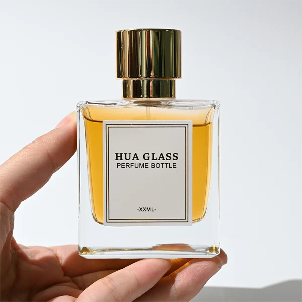 HUA0316 perfume bottle, square transparent colorless glass body with thick base and sharp edges, 30 ml, 50 ml, or 100 ml liquid, straight cylindrical Zinc Alloy cap or cylindrical cap with glossy gold bottle neck, printed label attached on bottle surface, modern minimalist luxury design, ideal for gifting and daily use.